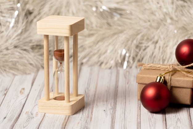 Foto sanduhr und pappschachtel auf einem holztisch verziert mit einer girlande und roten weihnachtsbällen für das neue jahr oder das weihnachten. post-, kurier- oder zustelldienstkonzept. kopieren sie platz