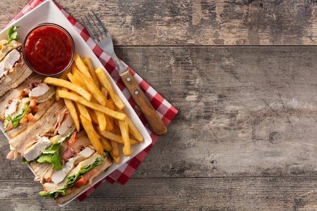 Sanduíche club e batatas fritas com molho de ketchup na mesa de madeira