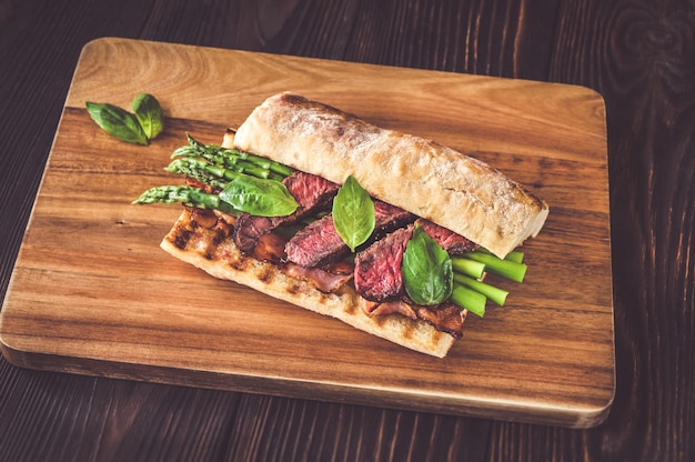 Sanduíche com aspargos e rodelas de bife na tábua de madeira