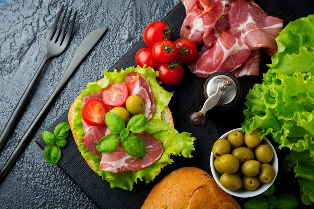 Sanduíche com carne seca, jamon com tomate cereja, manjericão, ciabatta, azeitonas no preto