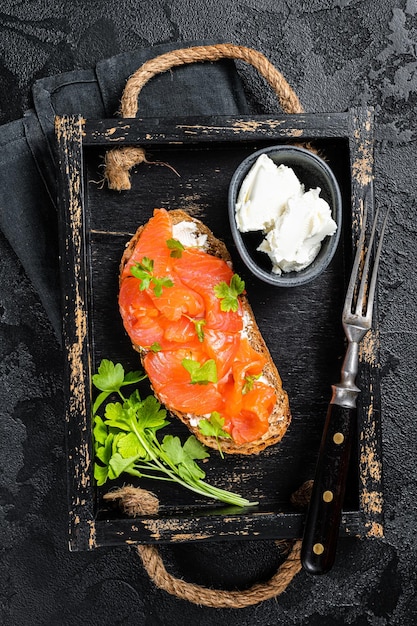 Sanduíche com filé de salmão e cream cheese na bandeja de madeira Fundo preto Vista superior