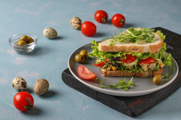 Sanduíche com frango, tomate cereja, ovos de codorna e microgreens contra um fundo azul claro