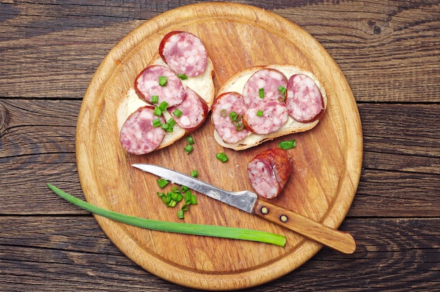 Sanduíche com linguiça e cebola verde em uma tábua redonda