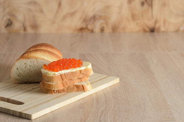 Sanduíche com manteiga e caviar vermelho em uma tábua com fatias de pão branco. Foco seletivo.