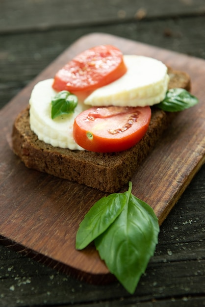 Sanduíche com queijo, tomate e manjericão em uma placa de madeira rústica. Comida saudável. Fundo alimentar