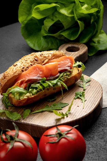 Sanduíche com salmão e rúcula servido em uma tábua de madeira em um fundo escuro