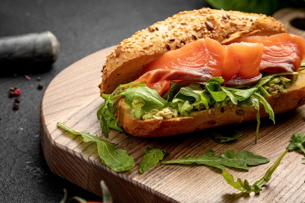 Sanduíche com salmão e rúcula servido em uma tábua de madeira em um fundo escuro