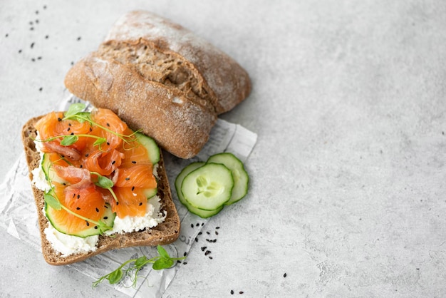 Sanduíche com sementes de pepino de salmão salgado e requeijão em uma mesa cinza