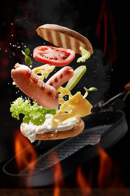 Sanduíche com tomate de queijo de salsichas e verde levitando sobre uma frigideira