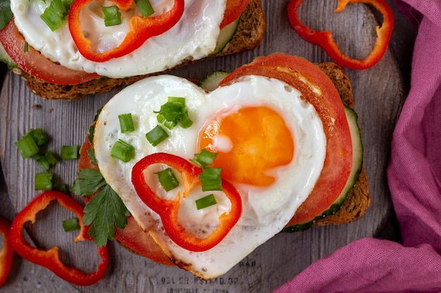 Sanduíche com tomate, pepino e ovo em forma de coração em uma placa de madeira, guardanapo roxo