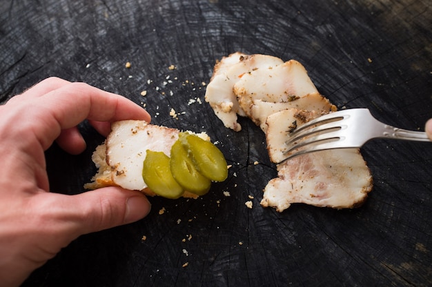 Sanduíche de bacon com pepino em conserva na mão masculina