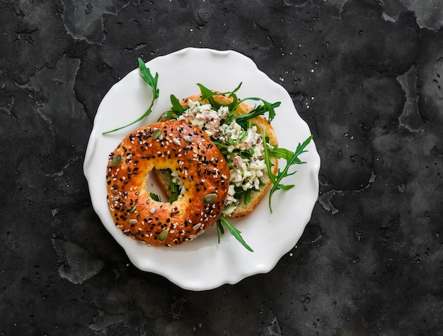 Sanduíche de bagel com salada de ovos de atum e rúcula delicioso lanche de pequeno-almoço em um fundo escuro vista superior