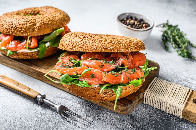 Sanduíche de bagels de salmão defumado com queijo macio e rúcula em uma tábua de cortar. Fundo branco. Vista do topo.