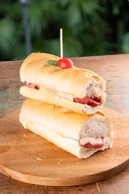 Sanduíche de baguete com mortadela e queijo mussarela e tomate cereja em uma mesa de madeira com fundo desfocado