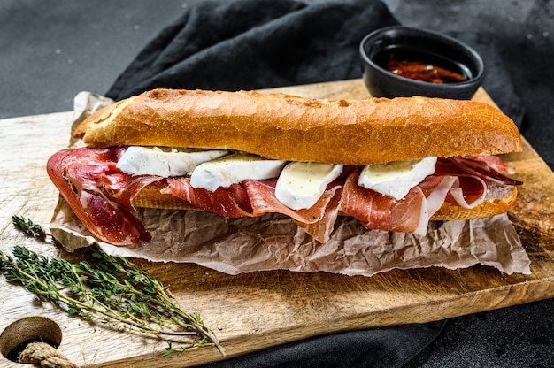 Sanduíche de baguete com presunto, queijo camembert em uma placa de corte.