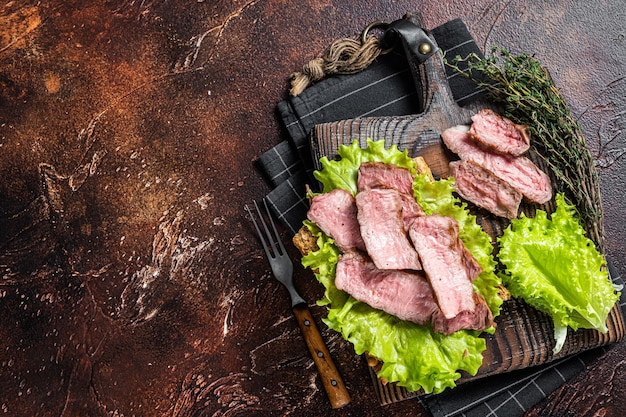 Sanduíche de bife com rosbife fatiado, salada e legumes. Fundo escuro. Vista do topo. Copie o espaço.