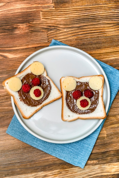 Sanduíche de cara de urso engraçado torrar pão com manteiga de amendoim, queijo e framboesa no fundo de madeira do guardanapo de prato. Crianças criança doce sobremesa café da manhã almoço comida close-up