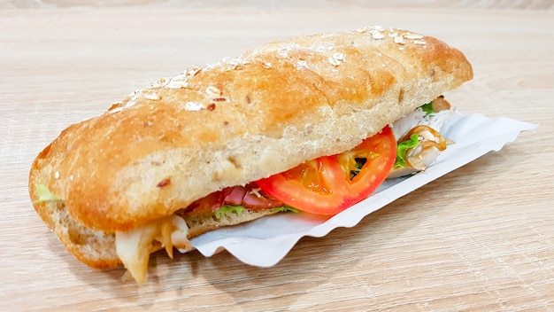 Sanduíche de ciabatta com alface, frango e queijo em uma mesa de madeira.