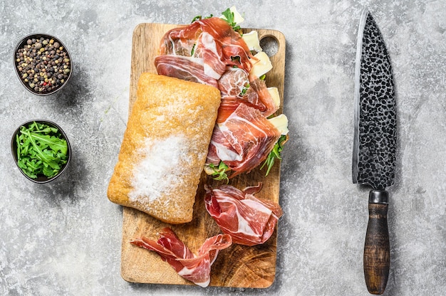 Sanduíche de ciabatta com presunto crudo de presunto, rúcula e queijo brie de camembert. Plano de fundo cinza. Vista do topo.