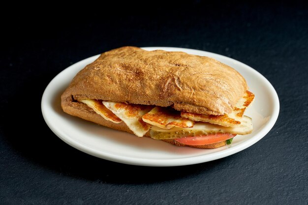 Sanduíche de ciabatta com queijo grelhado e vegetais em prato branco sobre fundo preto