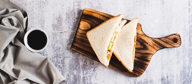 Foto sanduíche de clube com tomate de carne de frango e alface em uma tábua na mesa
