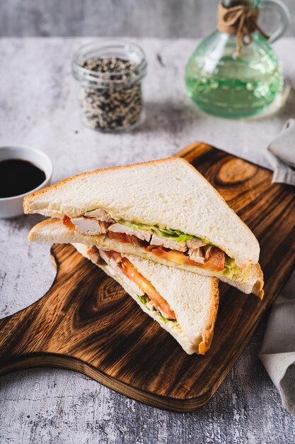 Foto sanduíche de clube com tomate de carne de frango e alface em uma tábua na vista vertical da mesa