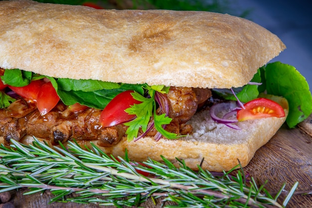 Sanduíche de costela de porco com tomate, rúcula e cebola roxa na mesa de madeira