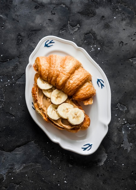 Sanduíche de croissant com banana de manteiga de amendoim em uma vista superior de fundo escuro