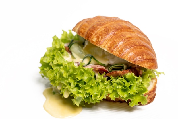 Sanduíche de croissant com queijo de carne e salada em um prato branco closeup vista lateral Isolado no fundo branco Menu de restaurante de conceito de café da manhã saudável