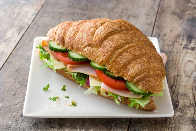 Sanduíche de croissant com queijo, presunto e legumes na mesa de madeira