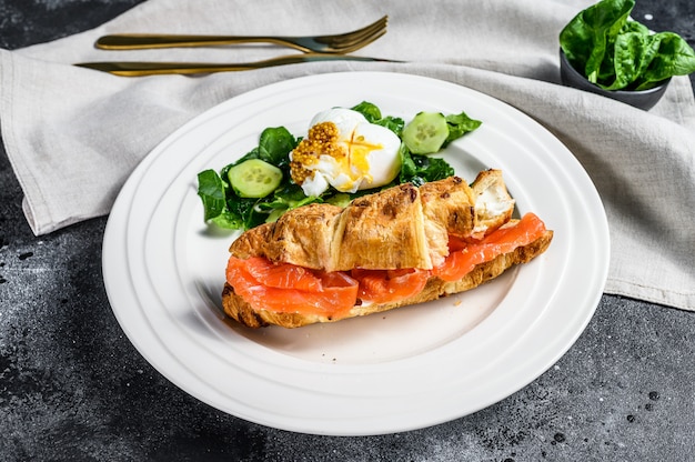 Sanduíche de croissant com salmão salgado servido com salada fresca deixa espinafre, ovo e legumes. Superfície preta. Vista do topo