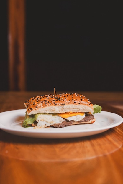 Sanduíche de filé com ovo frito e alface em um prato em uma mesa de madeira