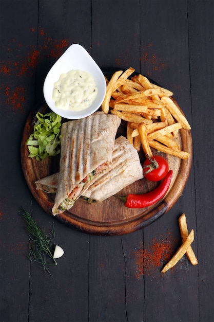 Foto sanduíche de frango grelhado com batatas fritas e picante em fundo de madeira