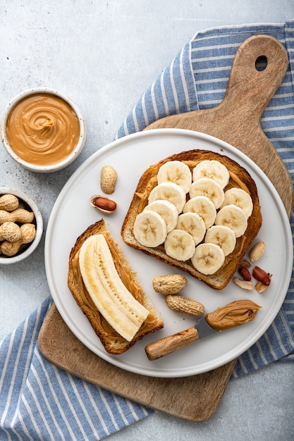 Sanduíche de manteiga de amendoim e banana em um prato branco sobre fundo cinza, vista superior