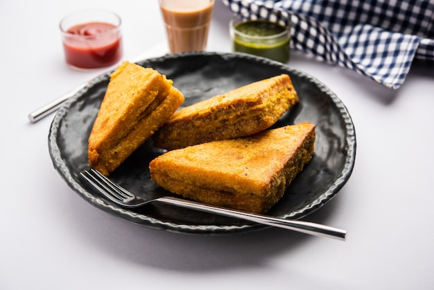 Sanduíche de pão Pakora ou pakoda em forma de triângulo servido com ketchup de tomate, chutney verde, lanche indiano popular na hora do chá