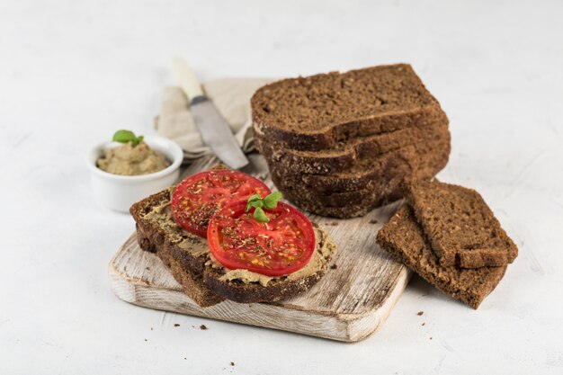 Sanduíche de pão preto com tomate e homus em uma placa de madeira