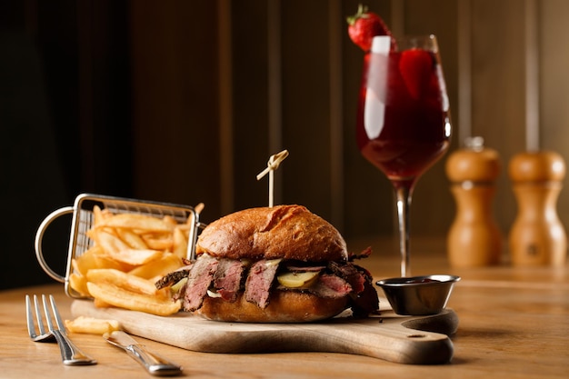 Foto sanduíche de pastrami no pão de centeio servido com picles e molho de mostarda saboroso sanduíche com batatas fritas e bebida de sangria em fundo escuro