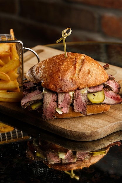 Sanduíche de pastrami no pão de centeio servido com picles e molho de mostarda Saboroso sanduíche com batatas fritas em fundo escuro