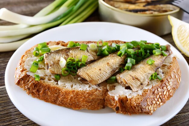 Sanduíche de peixe com espadilha, manteiga e cebolinha no prato branco, close-up