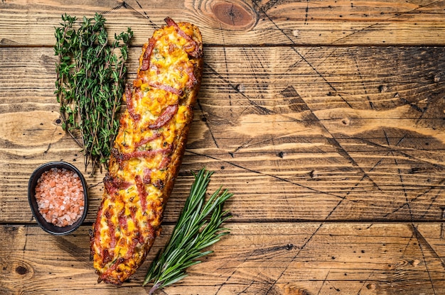 Sanduíche de pizza no pão baguete com presunto, bacon, legumes e queijo na mesa de madeira. fundo de madeira. Vista do topo. Copie o espaço.