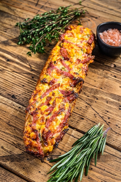 Sanduíche de pizza no pão baguete com presunto, bacon, legumes e queijo na mesa de madeira. fundo de madeira. Vista do topo.