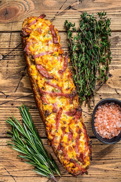 Sanduíche de pizza no pão baguete com presunto, bacon, legumes e queijo na mesa de madeira