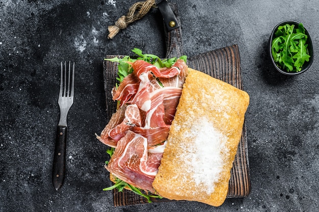 Sanduíche de presunto ibérico com pão ciabatta. Fundo preto. Vista do topo.