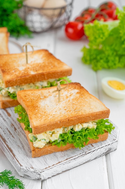 Sanduíche de salada de ovo com pão torrado e alface em um fundo branco de madeira. Foco seletivo