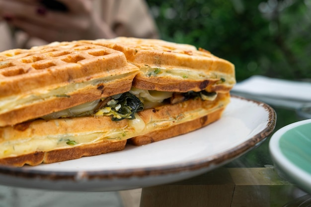 Sanduíche de waffle vegetariano belga com cogumelos espinafre e queijo em um prato ao ar livre no café de calçada