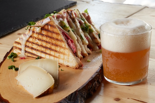 Foto sanduíche e queijo em uma bandeja de madeira com uma cerveja