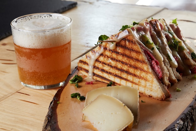 Sanduíche e queijo em uma bandeja de madeira com uma cerveja