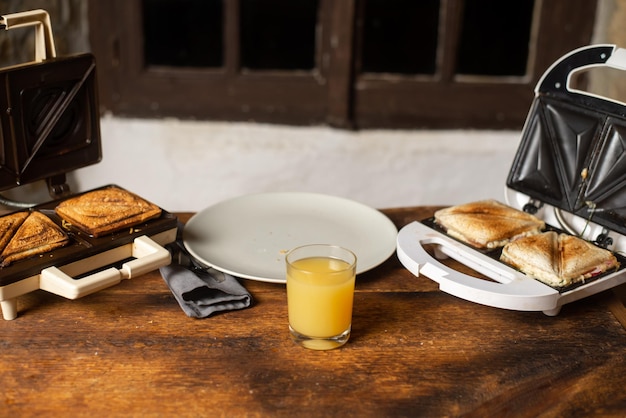 Sanduíche e suco Preparação de lanche e café da manhã Sanduicheira e prato vazio em fundo de madeira