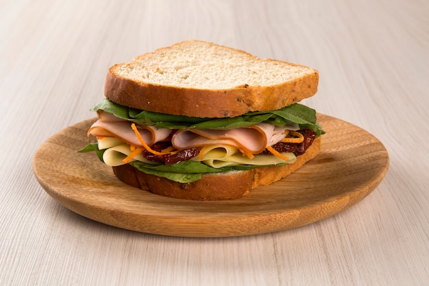 Foto sanduíche em um prato branco com peito de peru, tomate, alface e queijo na mesa