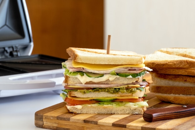 Foto sanduíche fresco com queijo, ervas, tomate, pepino e bacon na mesa de madeira com pão.